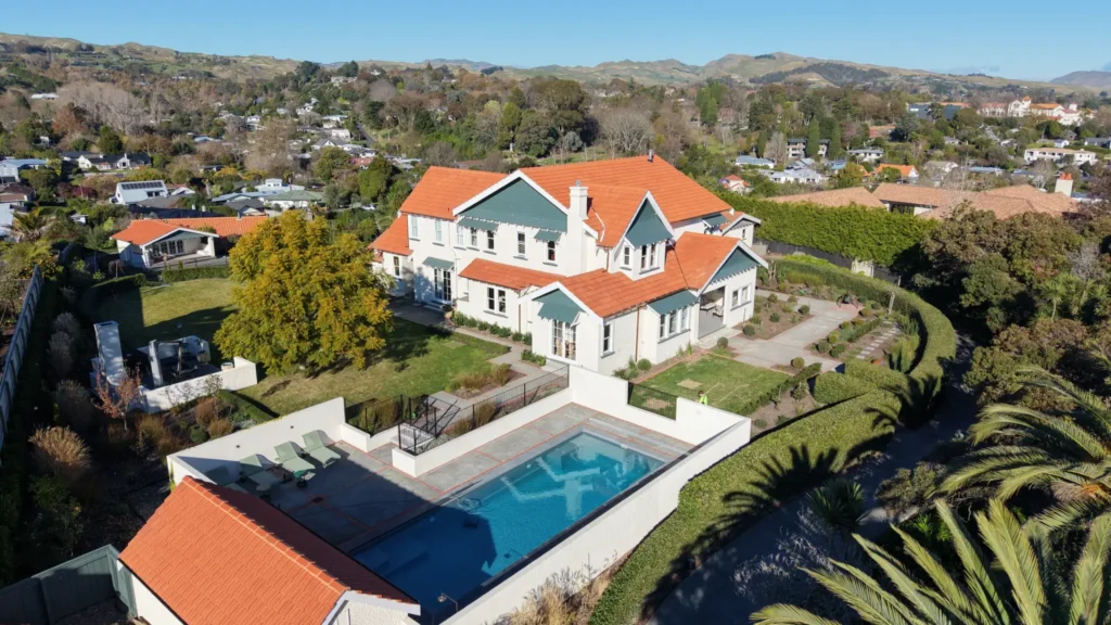 Aerial view of a two-storey white home with a red roof, swimming pool and gardens